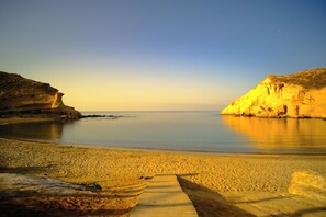 A beach with a wooden walkway leading to the water, surrounded by rocky cliffs. - Maxcaly Playa by Blossom Hotels (Aguilas)