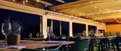Un área de comedor al aire libre con mesas y sillas, luces colgantes y vistas al cielo nocturno.