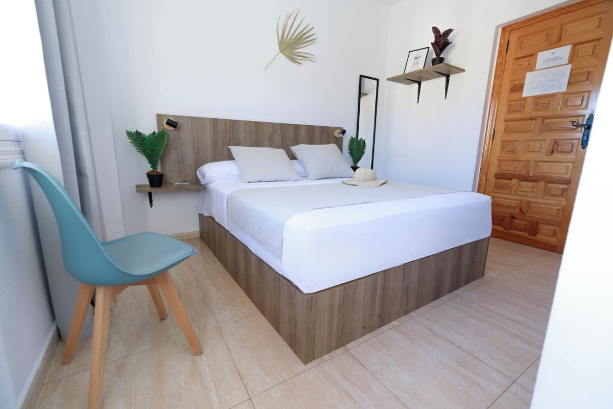 Une chambre à coucher avec une tête de lit en bois, un lit recouvert de draps blancs, une chaise bleue et une porte en bois.