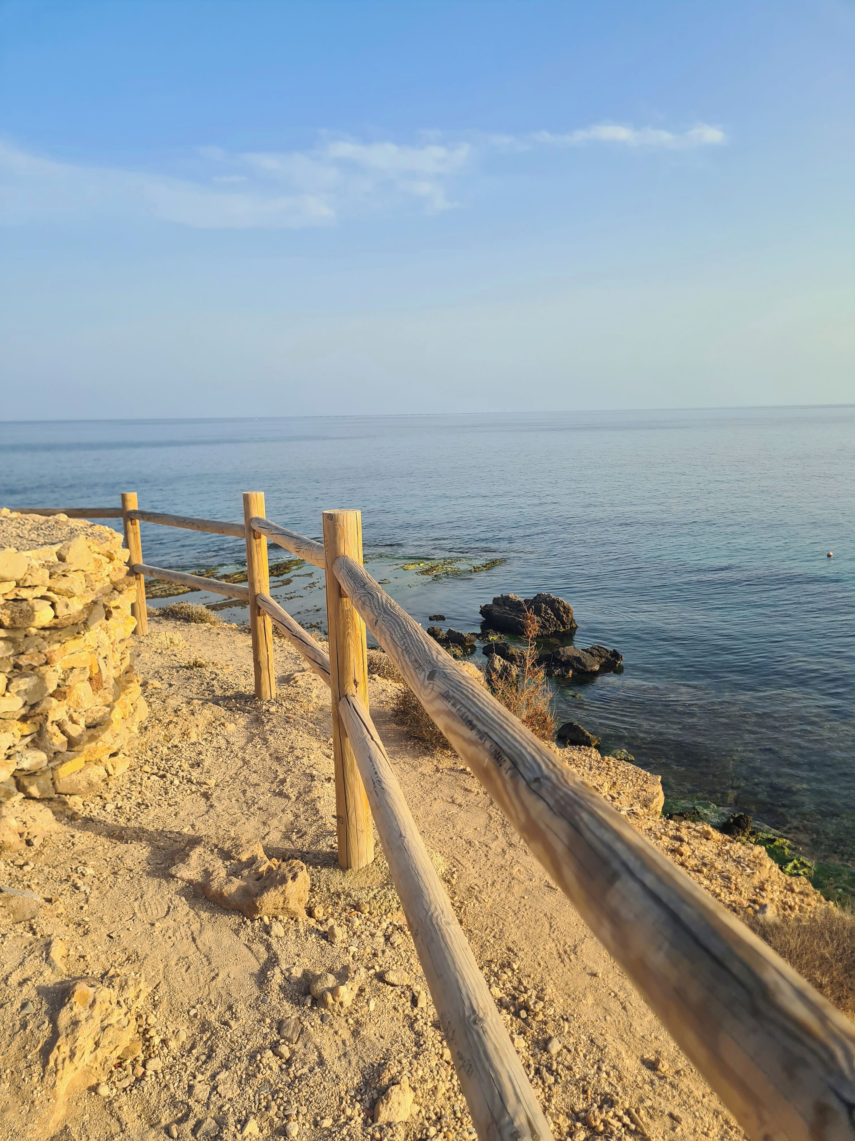 Una cerca de madera a lo largo de una costa rocosa con agua azul cristalina al fondo.
