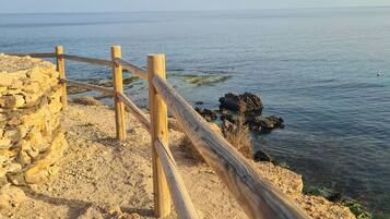 Una cerca de madera a lo largo de una costa rocosa con agua azul cristalina al fondo.