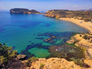 A coastal landscape with clear blue waters, rocky terrain, and a sandy beach. - Maxcaly Playa by Blossom Hotels (Aguilas)