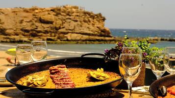 Paella mit Meeresfrüchten auf einem Tisch, mit Blick auf das Meer und eine felsige Klippe.