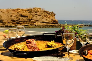 A seafood paella on a table with a view of the sea and a rocky cliff. - Maxcaly Playa by Blossom Hotels (Aguilas)