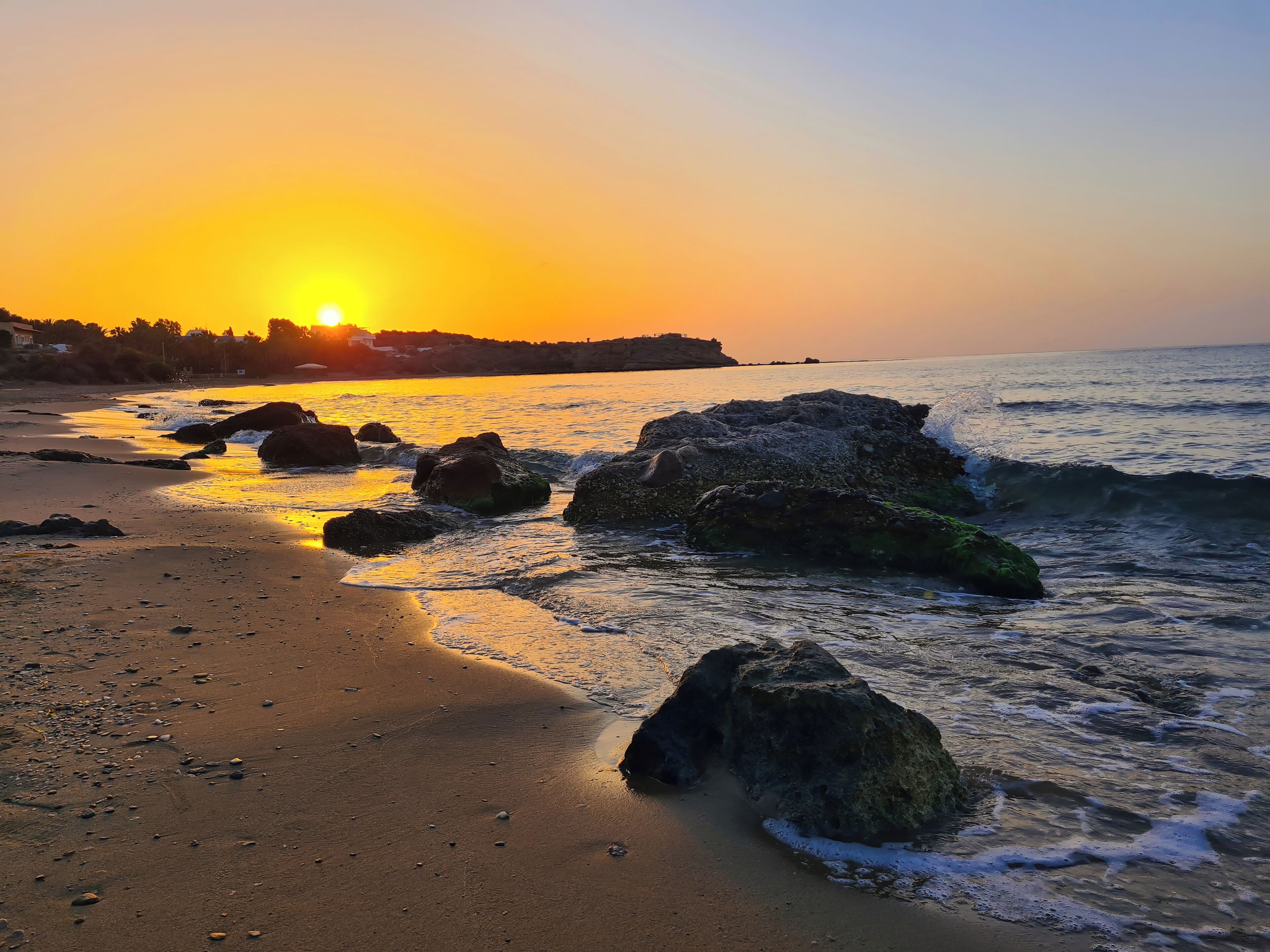 Una playa con rocas grandes y olas al atardecer.