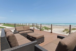 A deck with wicker furniture and a view of the beach.
