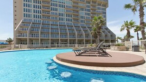 A swimming pool with lounge chairs and a palm tree, surrounded by a high-rise hotel building.