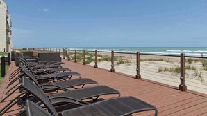 A wooden deck with rows of black lounge chairs facing the beach.
