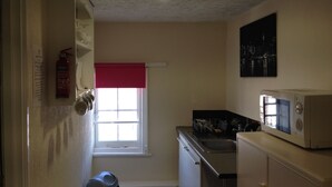 A compact kitchen with a microwave, sink, and window with a red valance. - Acapulco Rooms (Portsmouth)