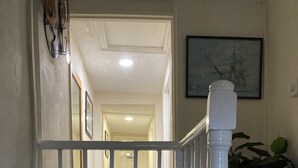 A hallway with a white railing, a door labeled "ROOM," and a framed picture on the wall. - Acapulco Rooms (Portsmouth)