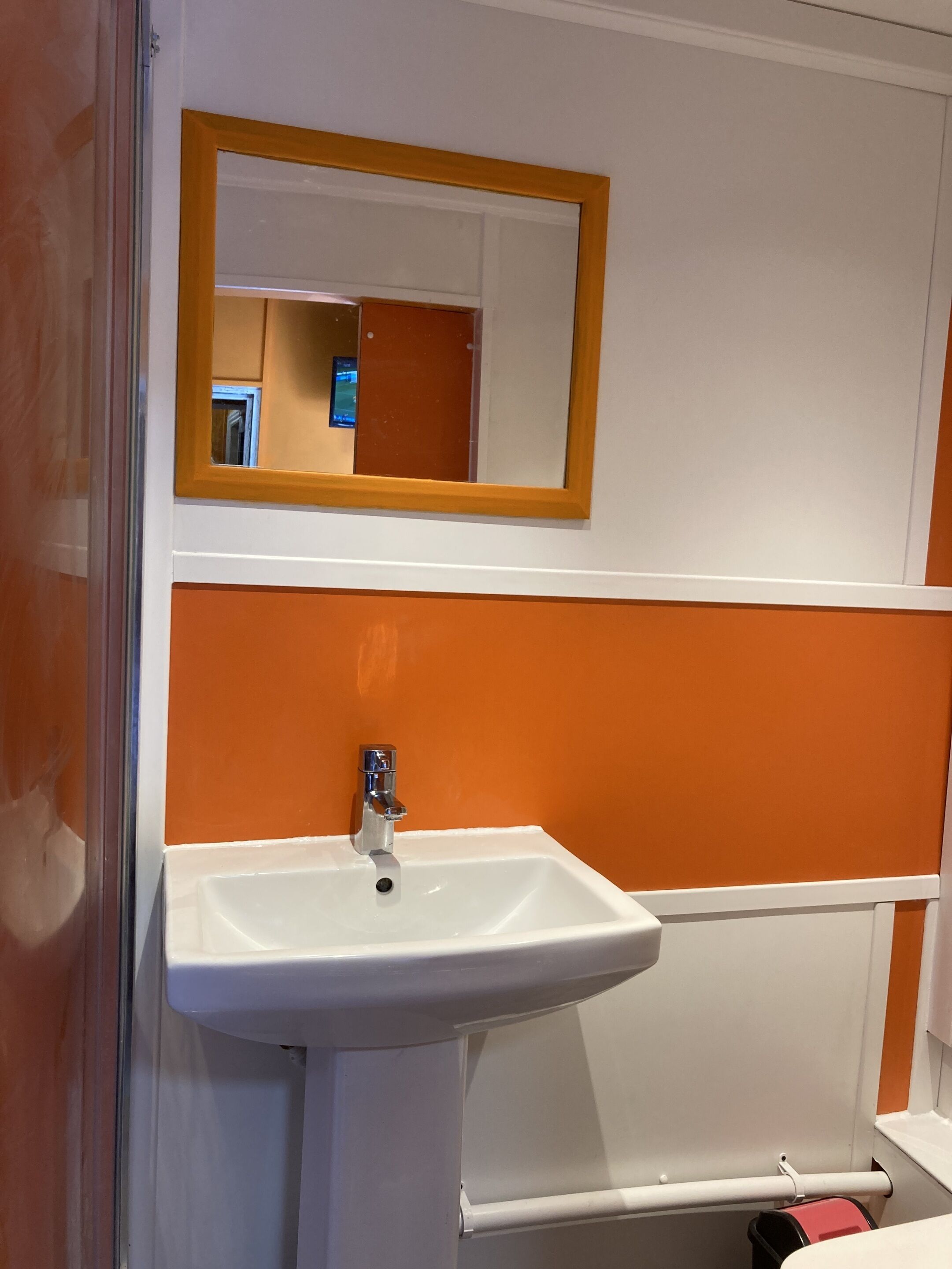 Un baño con un lavamanos blanco, un espejo con marco de madera y paredes anaranjadas.