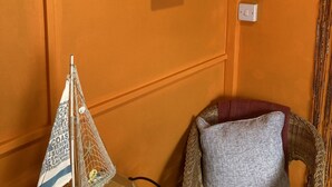 A room with an orange wall, a small sailboat model on a wooden tray, a wicker chair with a patterned cushion, and a sign advertising fresh and local oysters for sale. - Acapulco Rooms (Portsmouth)