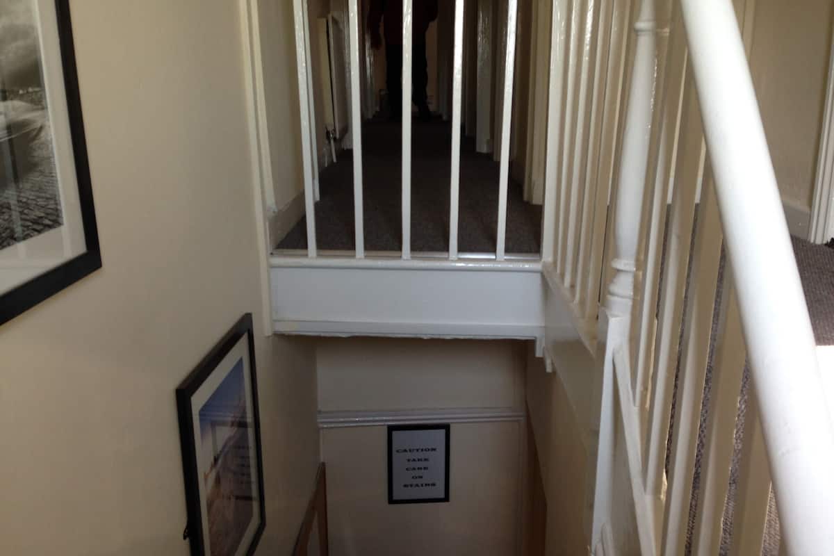 Ein schmaler Flur mit Treppe rechts, einem gerahmten Bild links und einem Warnschild an der Wand.