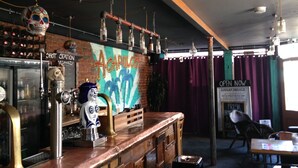 A bar area with a counter, shelves with bottles, a mural, and a sign indicating Sunday service. - Acapulco Rooms (Portsmouth)