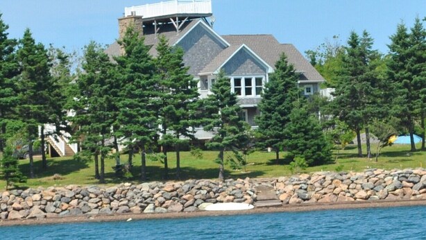 A large house with a stone wall and a dock extending into a body of water. - LUXURY HOME WITH GUEST HOUSE ON ACADIAN ISLAND ESTATE (Monastery)