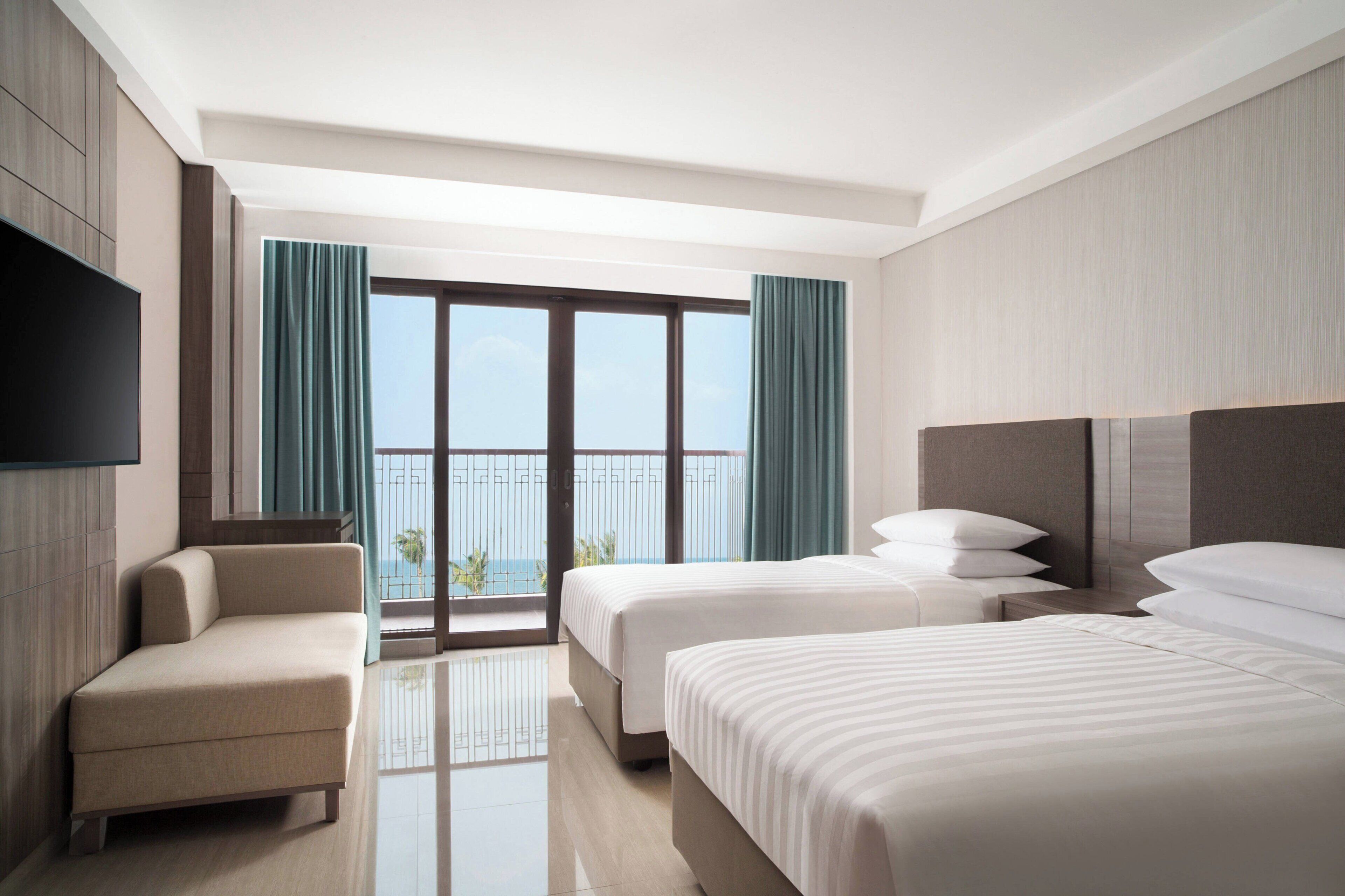 Una habitación de hotel con un ventanal grande, dos camas, un sofá y un televisor de pantalla plana.