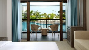 A hotel room with a balcony, a bed, a sofa, and a view of a pool and greenery. - Fairfield by Marriott Belitung (Tanjung Pandan)