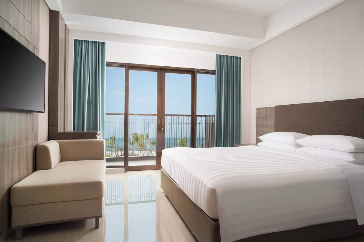 A modern hotel room with a large bed, a sofa, and a balcony with a view of the sea.