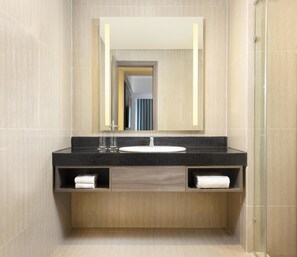 A modern bathroom with a black granite countertop, a white sink, and a mirror above. There are two towel slots and a wooden vanity.