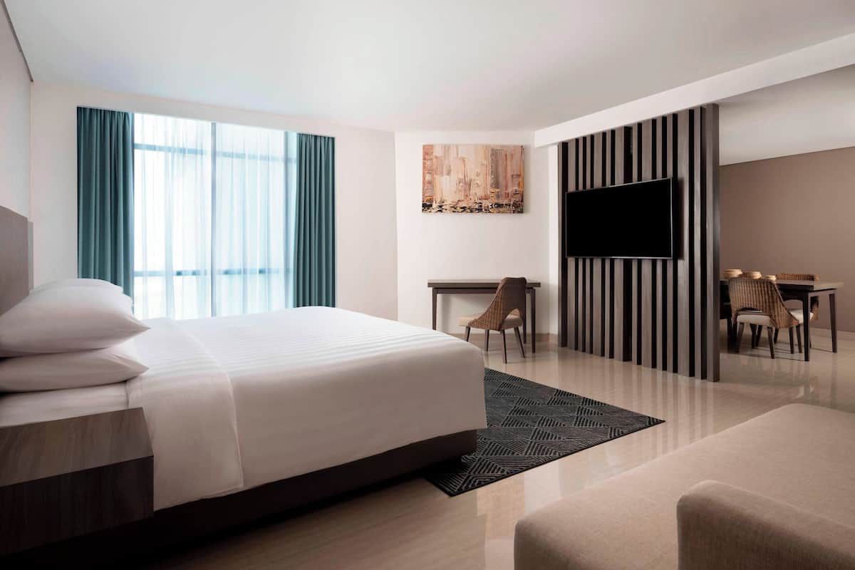 A modern hotel room with a large bed, a desk, a TV, and a seating area.