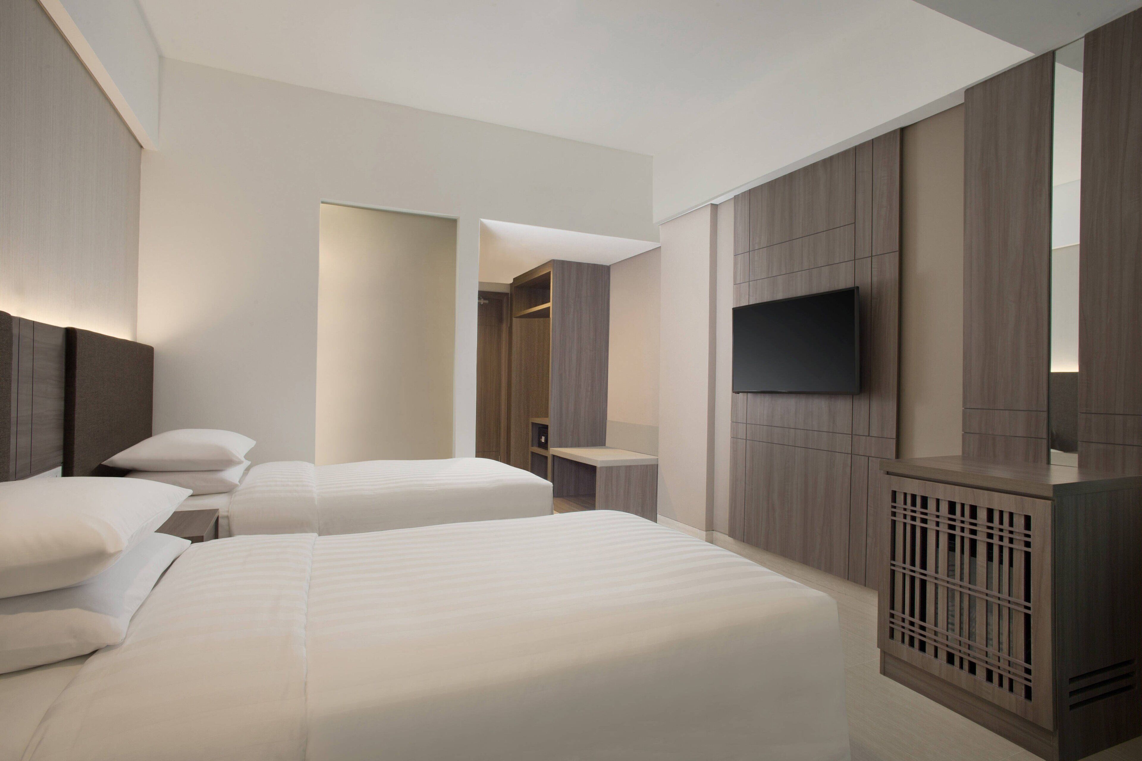 A modern hotel room with two beds, a TV, and a walk-in closet.