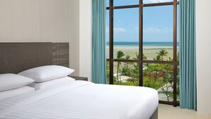 A hotel room with a large window offering a view of the beach and palm trees. - Fairfield by Marriott Belitung (Tanjung Pandan)