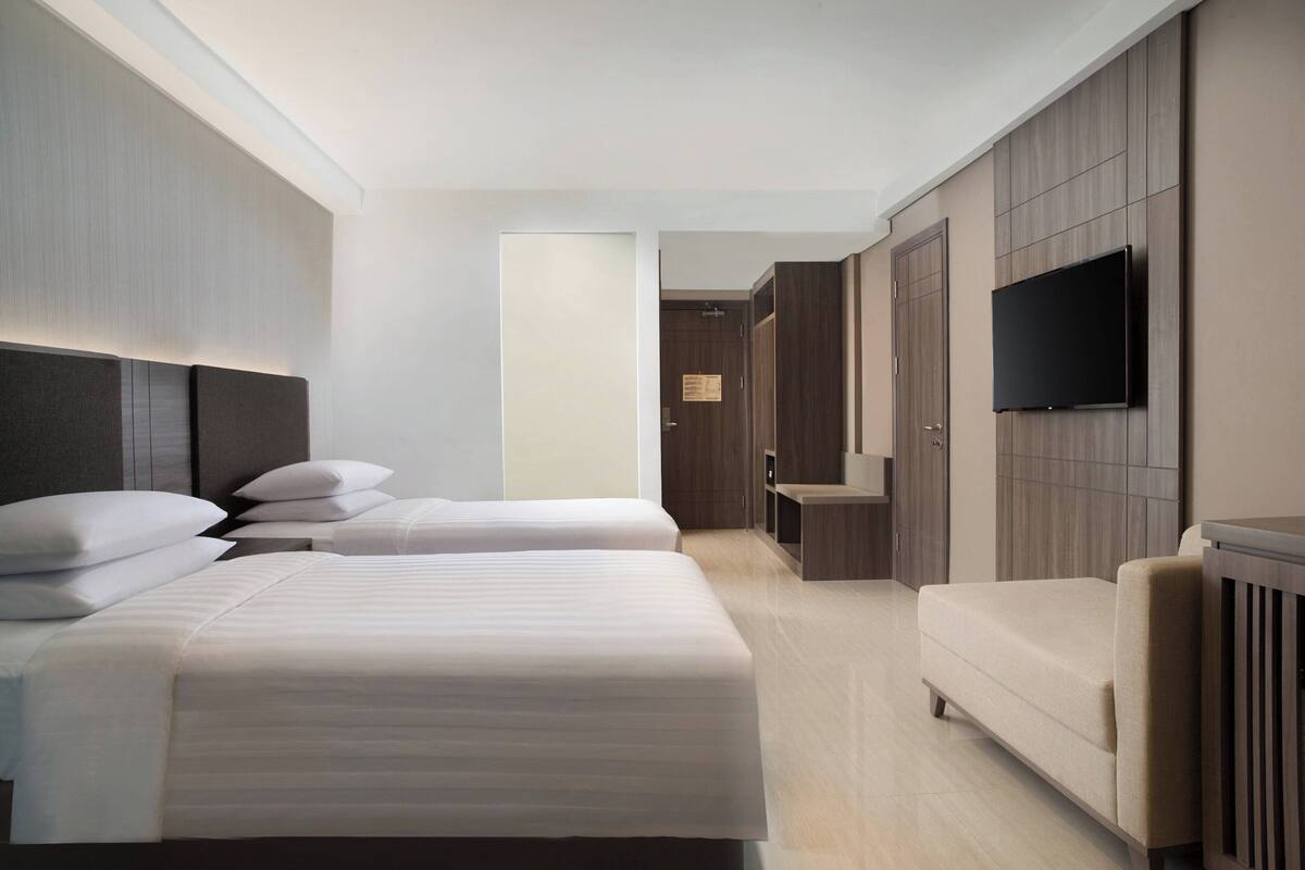 A modern hotel room with two beds, a sofa, a TV, and a wardrobe.