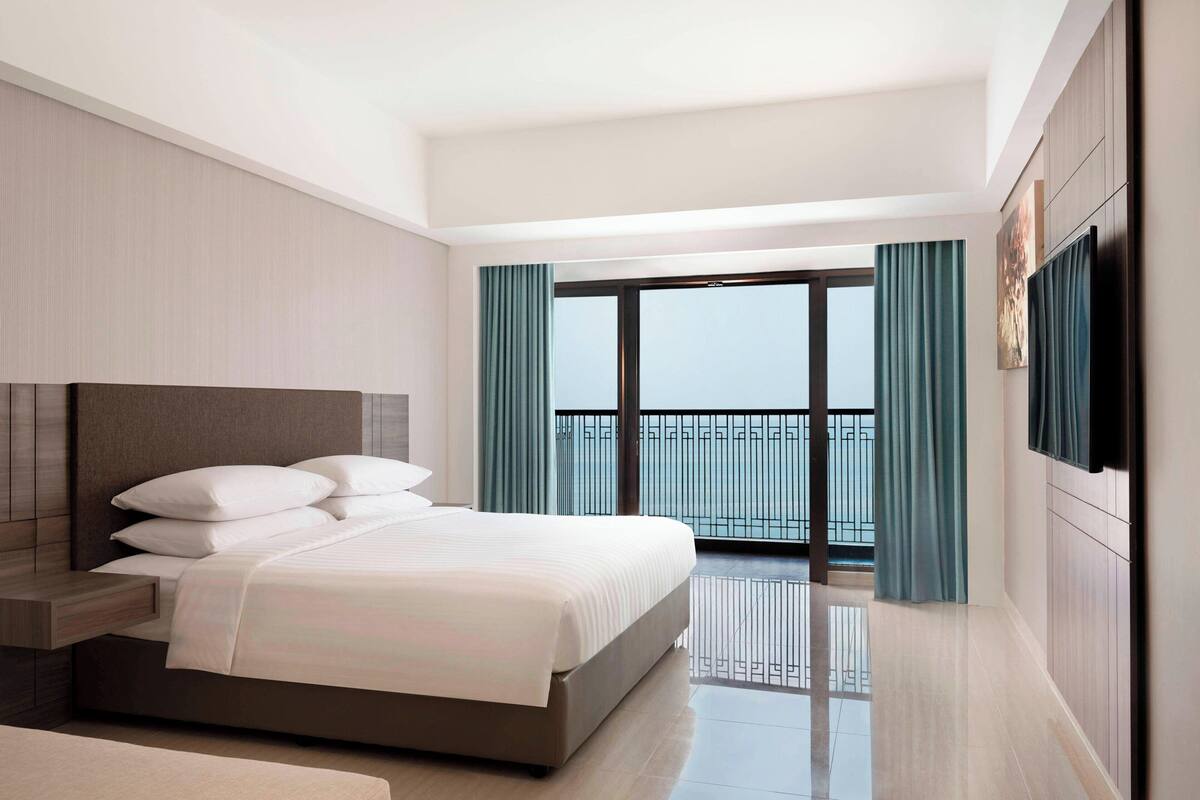 A modern hotel room with a large bed, a flat-screen TV, and a balcony with curtains.