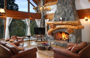 A spacious living room with leather sofas, a stone fireplace, and a large TV. - Apartments Bariloche - Villa Traful (Villa Traful)