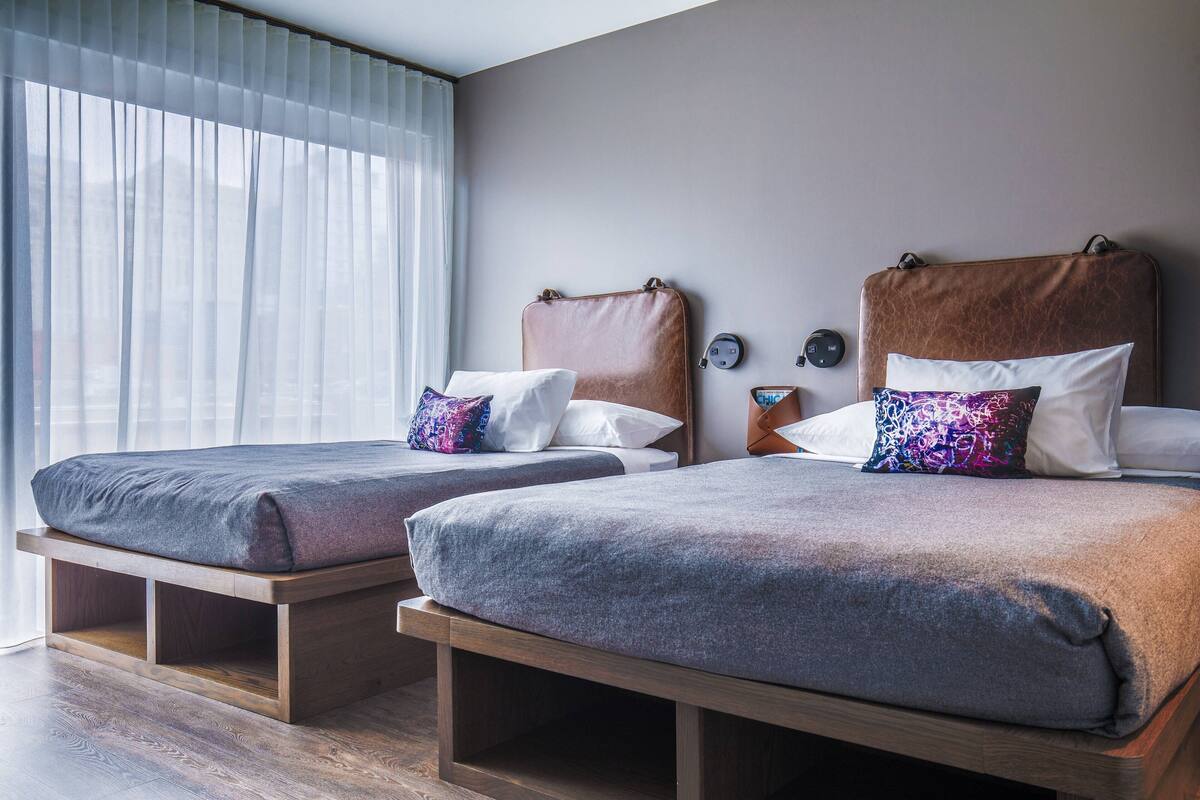 Una habitación de hotel con dos camas, cada una con cabecero de madera, mesita de noche y almohada.