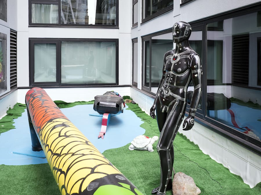 A room with a large window, a robotic figure, and a long, colorful object resembling a snake.