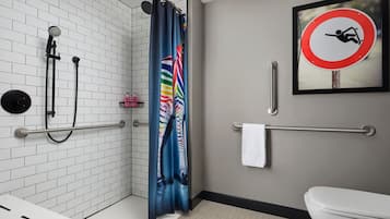 A modern bathroom with white tiled walls, a shower with a rain showerhead, a colorful shower curtain, a handrail, a toilet, and a no slip sign on the wall.