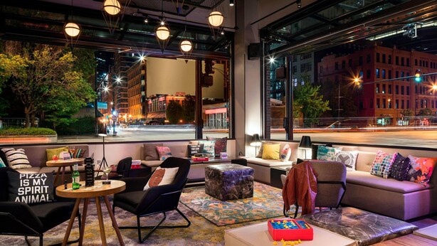 Un área de descanso moderna con asientos, una mesa de centro y vistas de la ciudad por la noche.