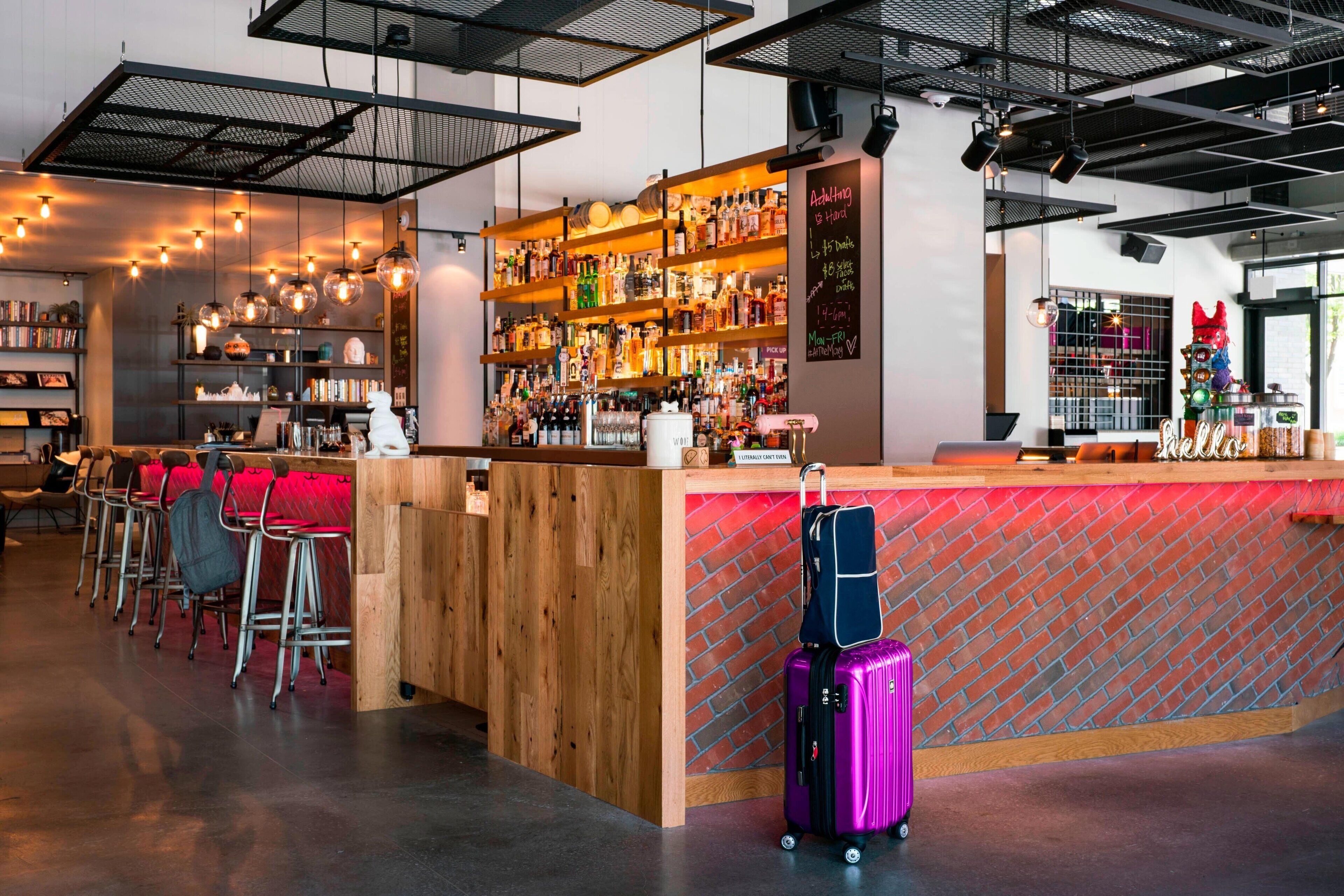 Una zona de bar con mostrador de madera, taburetes y una variedad de botellas y vasos.