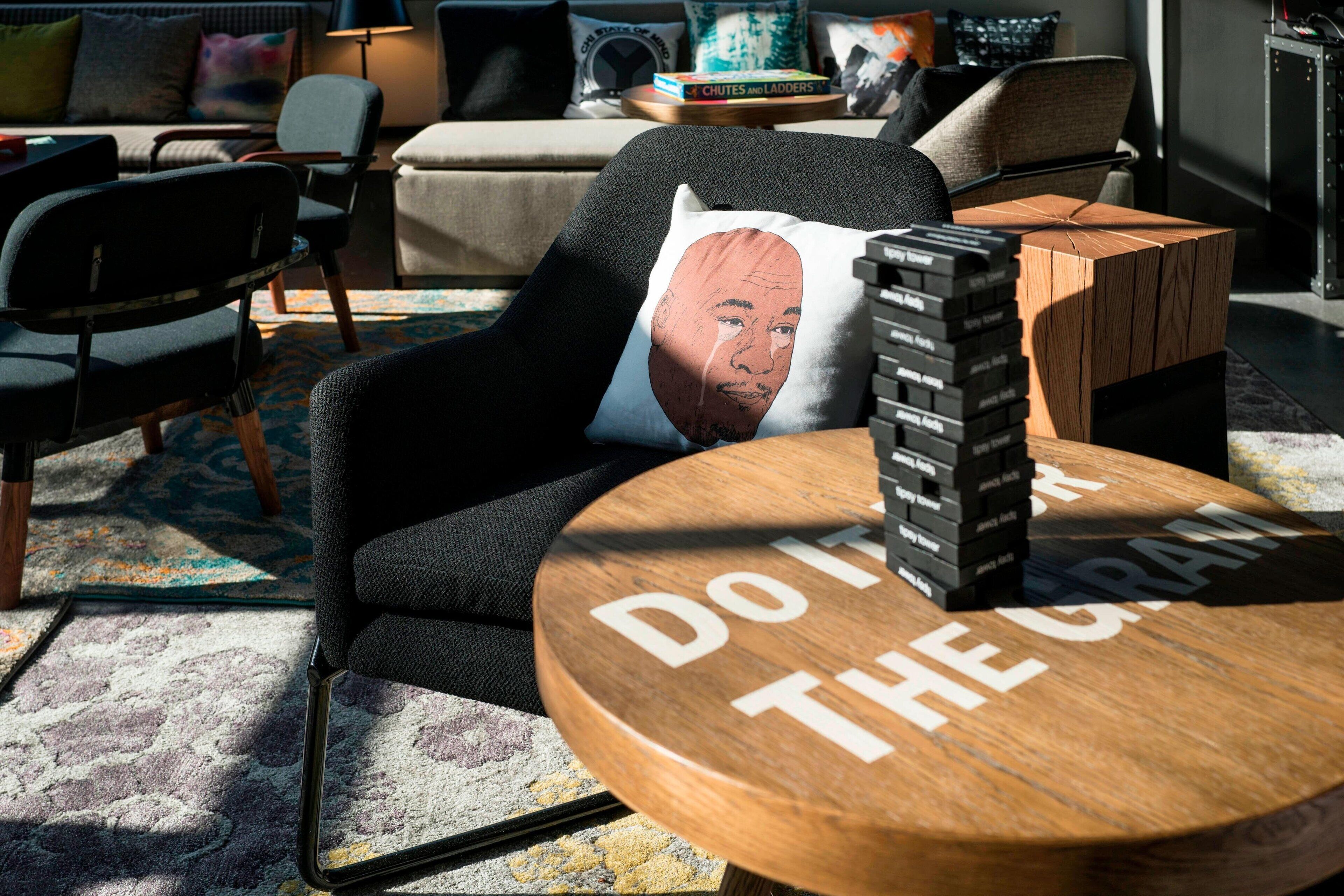 Una sala de estar moderna con una mesa de centro redonda de madera, un sillón negro y un sofá con cojines estampados.