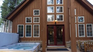 A wooden lodge with a hot tub, a front door, and a porch with seating. - Sawmill Run Lodge: Pet-Friendly, Walk to Peak 8, Hot Tub, Grill, Shuttle (Breckenridge)