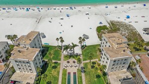 Ein Luftbild eines Hotels mit Strand, das einen zentralen Innenhof mit einem Tennisplatz zeigt, umgeben von Gebäuden mit Balkonen mit Blick auf den Strand.