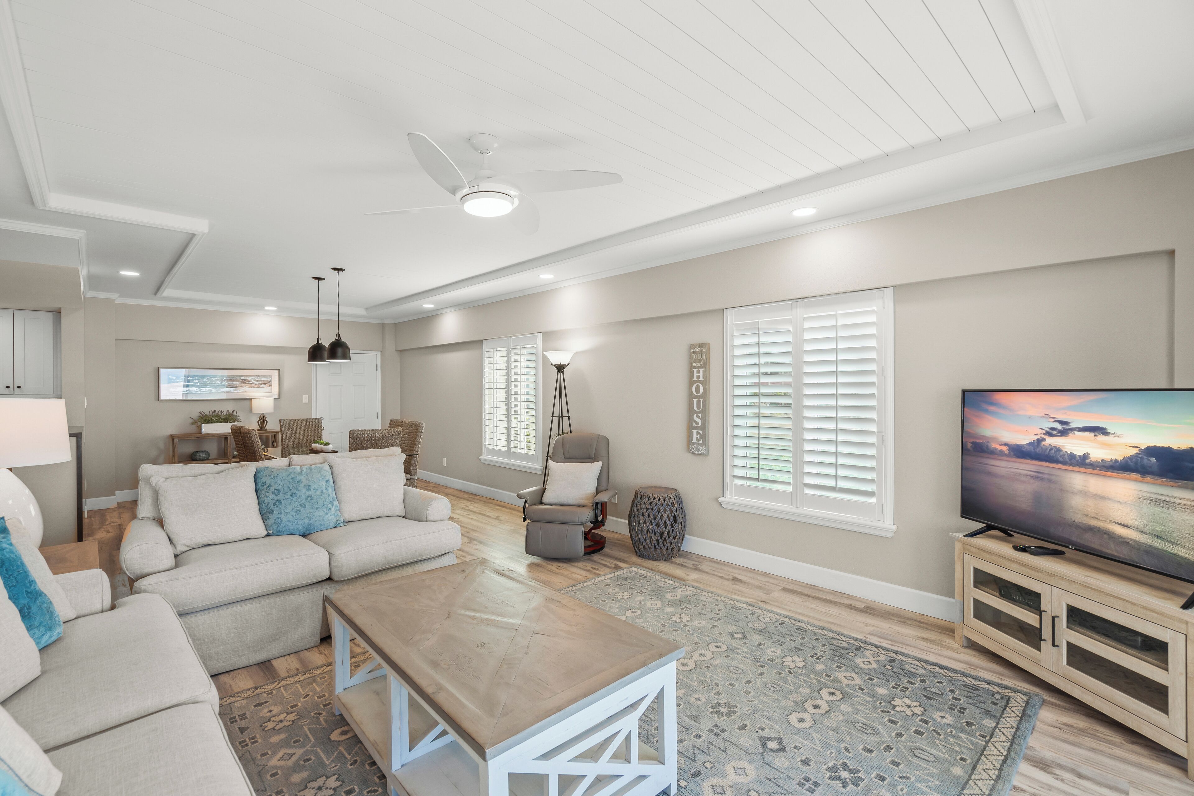 A spacious living room with a large flat-screen TV, a ceiling fan, and a wooden coffee table.