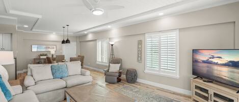 A spacious living room with a large flat-screen TV, a ceiling fan, and a wooden coffee table.