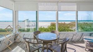 A sunlit room with a large glass window overlooking a beach, wicker furniture, and a ceiling fan. - Island House Beach Resort 1N (Siesta Key)