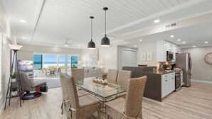 A modern kitchen with white cabinets, a stainless steel refrigerator, and a dining area with wicker chairs and a glass table. - Island House Beach Resort 1N (Siesta Key)