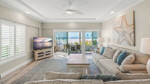 A spacious living room with a large television, a comfortable sofa, and a dining area with a view of the ocean. - Island House Beach Resort 1N (Siesta Key)