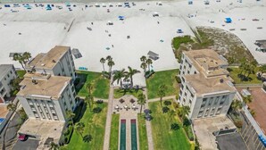 An aerial view of a beachfront hotel with multiple buildings, a sandy beach with umbrellas, and a central green area with a pool. - Island House Beach Resort 1N (Siesta Key)