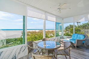 Una habitación luminosa con una mesa de vidrio y sillas de mimbre, con vistas a una playa y el océano.