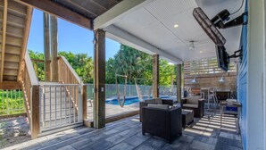 Um alpendre coberto com piscina, móveis de vime e vista para a área da piscina.