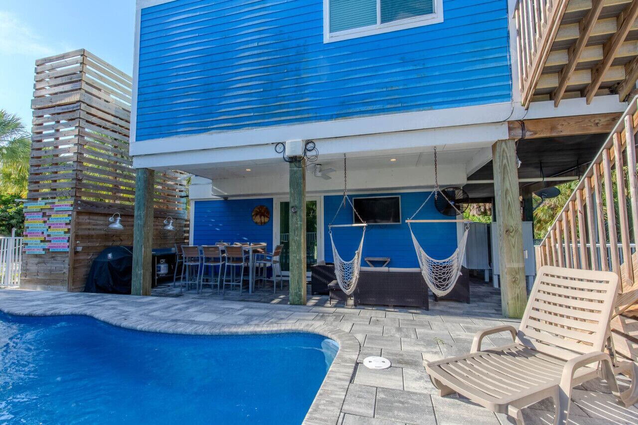 Un edificio azul con piscina, mobiliario exterior y una hamaca.