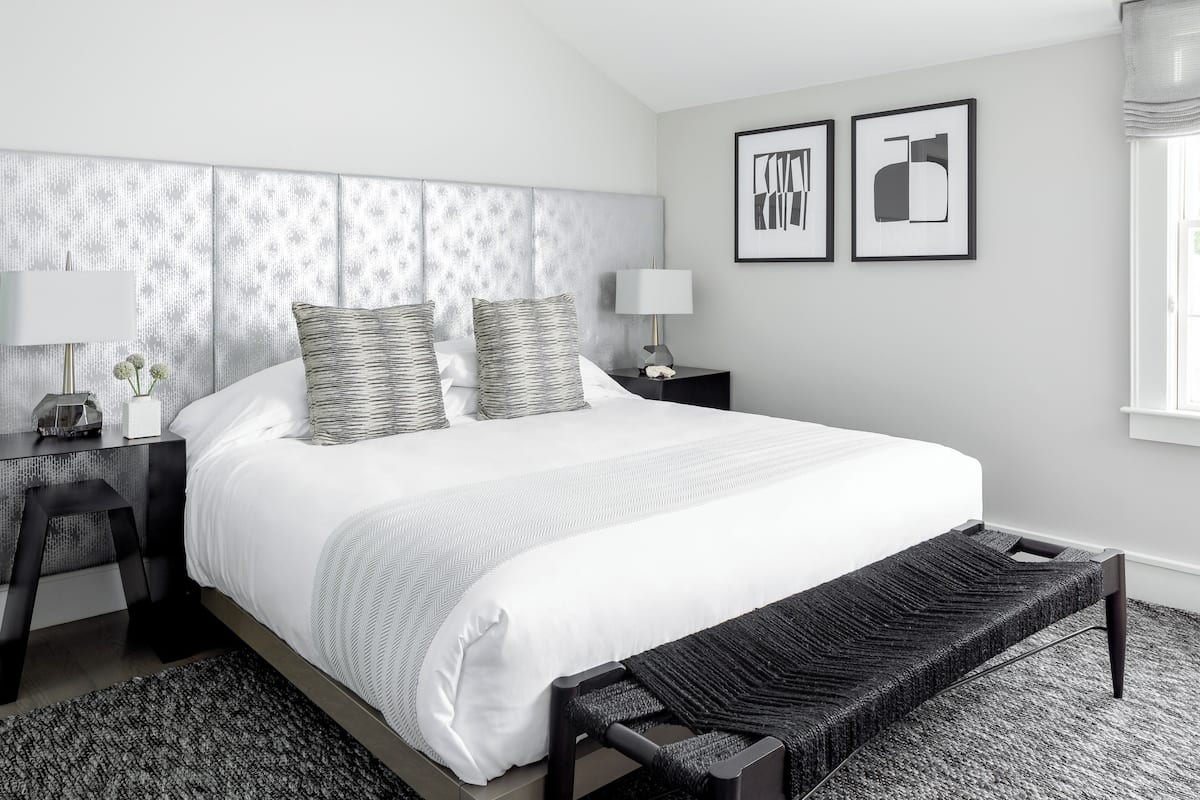 Une chambre à coucher moderne avec un grand lit, deux tables de chevet, un banc et deux tableaux encadrés accrochés au mur.