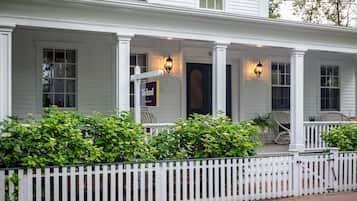 Stunning two-story home with a covered porch and white columns, surrounded by lush greenery and a charming picket fence.