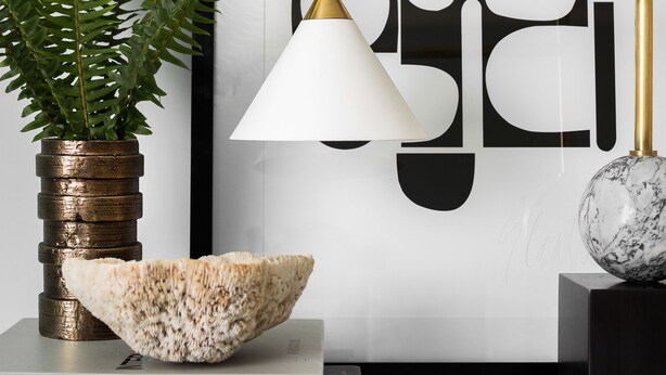 A framed artwork with abstract figures, a potted plant, a white bowl, and a lamp on a shelf. - The Richard, The Edgartown Collection (Edgartown)