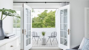 A room with a large open door leading to a balcony with two chairs and a table, a potted plant, and a grey sofa with a patterned pillow. - The Richard, The Edgartown Collection (Edgartown)